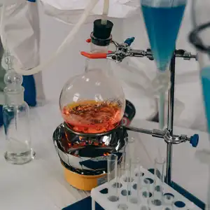 Laboratory distillation setup with a round-bottom flask heated by a mantle, connected to a condenser with cooling water flow, and a separatory funnel adding liquid reagent.