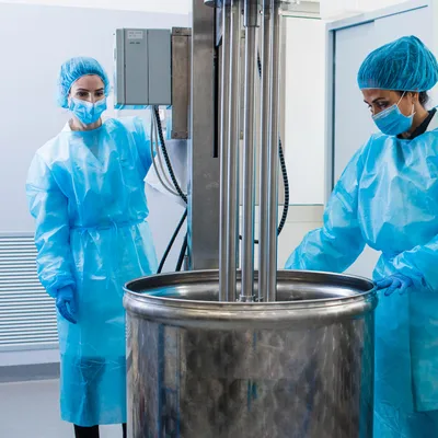 Chemical engineers in protective clothing working with stainless steel mixing tank in a pharmaceutical plant